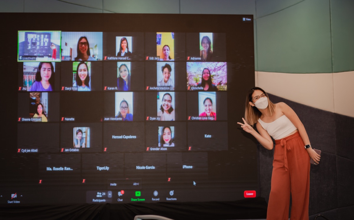 Demi beside a wall of students joining the event on Zoom